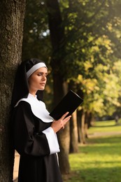 Young nun reading Bible in park on sunny day