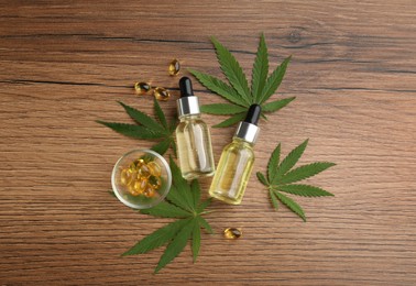 Composition with CBD oil, THC tincture and hemp leaves on wooden table, flat lay