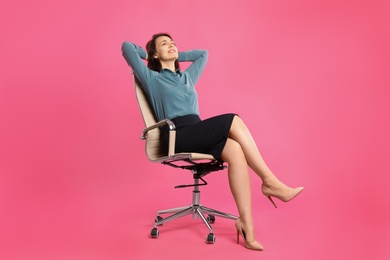Photo of Mature businesswoman relaxing in comfortable office chair on pink background
