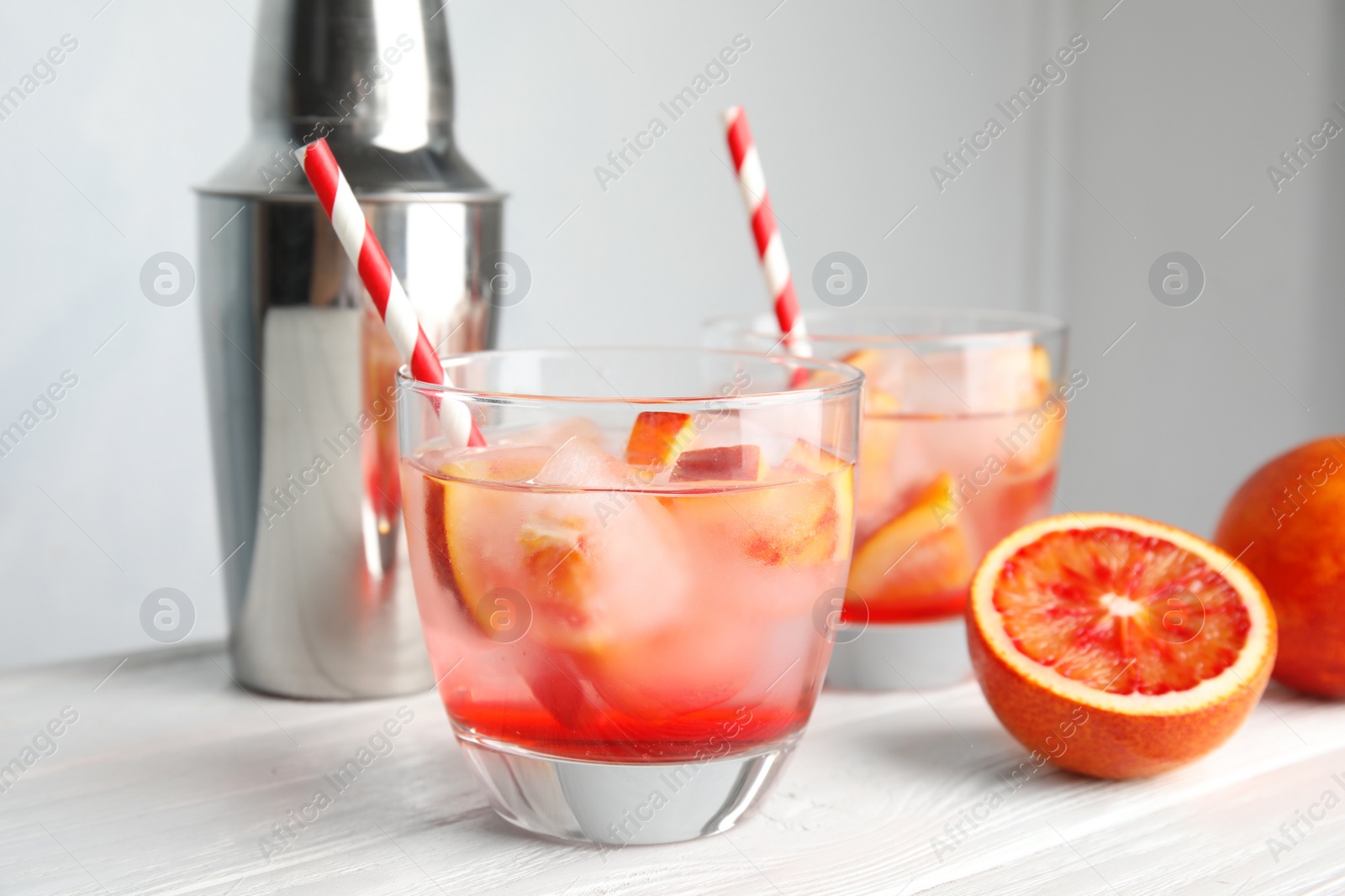 Photo of Glass of tropical cocktail with ice cubes on table against light background