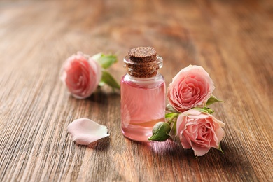 Photo of Bottle of rose essential oil and flowers on wooden table