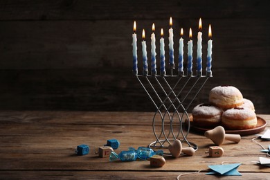 Photo of Hanukkah celebration. Menorah with burning candles, dreidels and donuts on wooden table, space for text