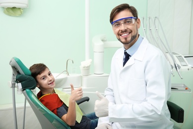 Photo of Professional dentist and happy little patient in modern clinic