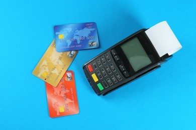 Photo of New modern payment terminal and credit cards on light blue background, flat lay