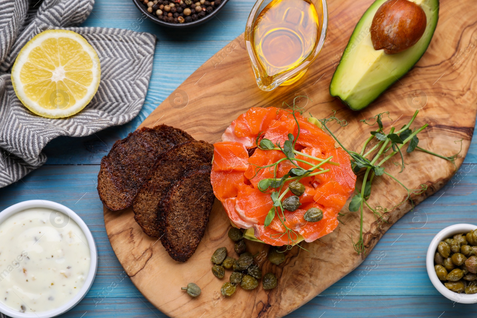 Photo of Delicious salmon tartare with croutons on light blue wooden table, flat lay