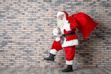 Authentic Santa Claus with big red bag full of gifts near brick wall