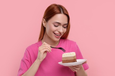 Young woman eating piece of tasty cake on pink background