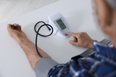 Man measuring blood pressure at table indoors, closeup