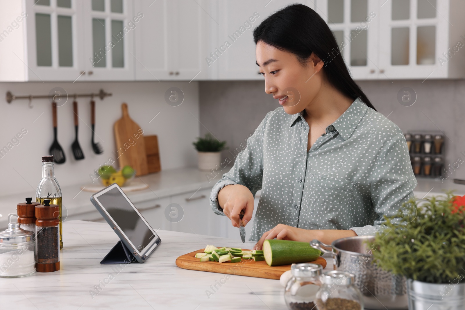 Photo of Beautiful woman looking at recipe on tablet while cooking in kitchen