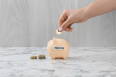 Photo of Pension savings. Woman putting coin into piggy bank at white marble table, closeup