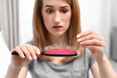 Photo of Emotional woman holding brush with fallen hair at home