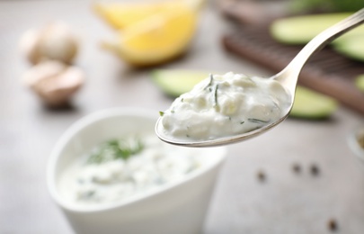 Photo of Spoon of cucumber sauce against blurred background, space for text. Traditional Tzatziki