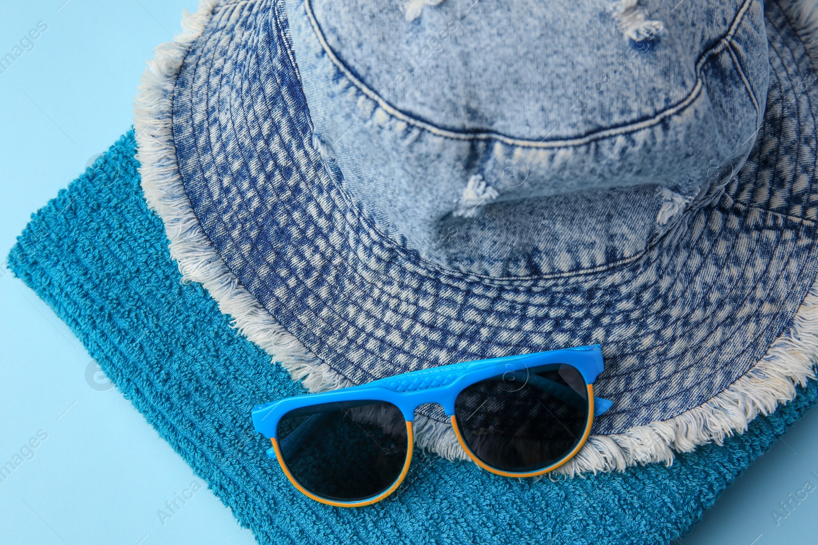 Photo of Towel, denim hat and sunglasses on light blue background, flat lay. Beach accessories