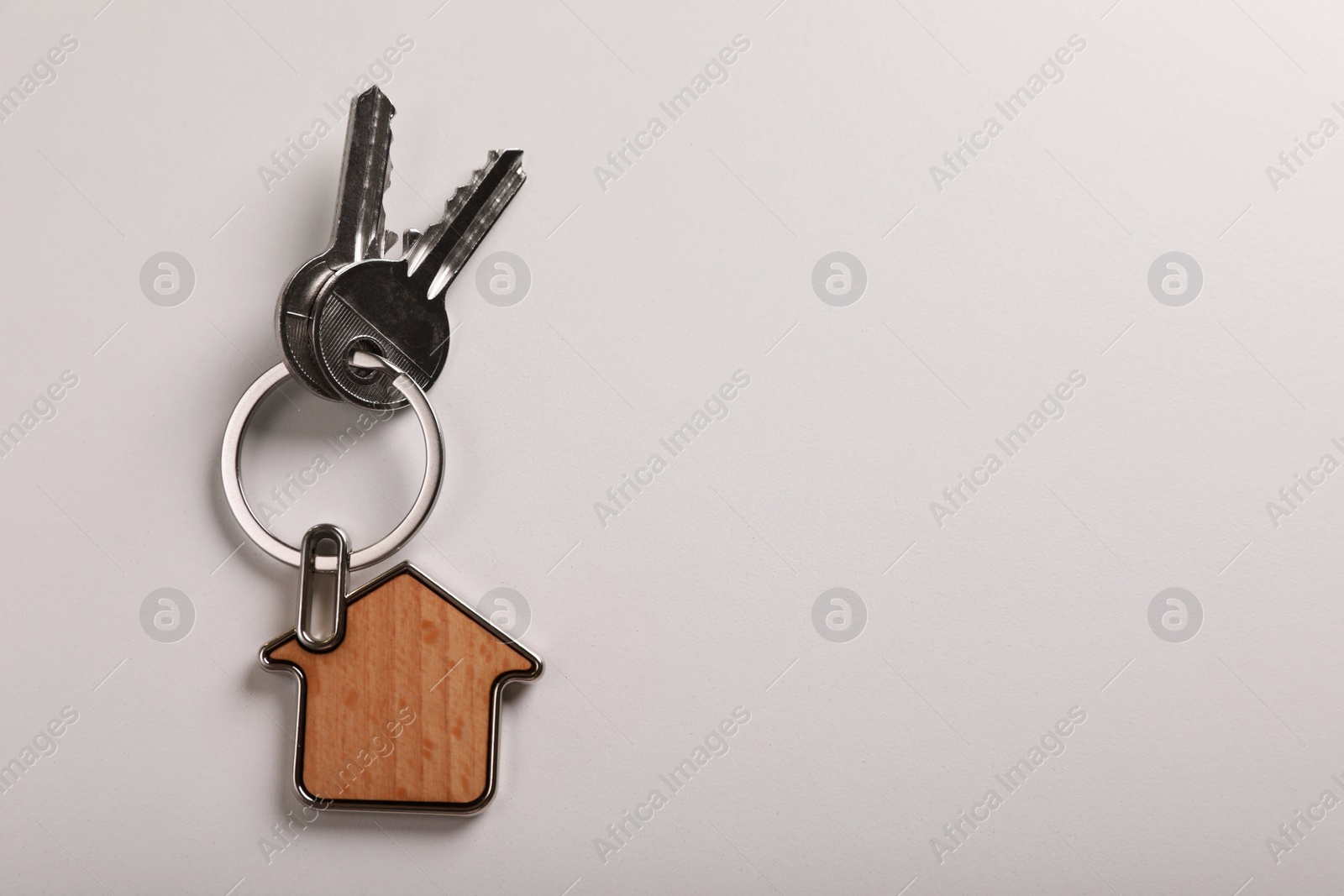 Photo of Keys with trinket in shape of house on white background, top view and space for text. Real estate agent services