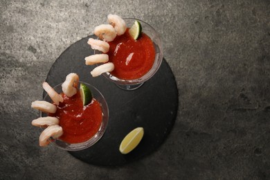 Photo of Tasty shrimp cocktail with sauce in glasses and lime on grey table, flat lay. Space for text