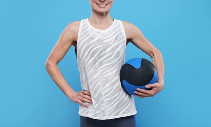 Photo of Sportswoman with medicine ball on light blue background, closeup. Space for text