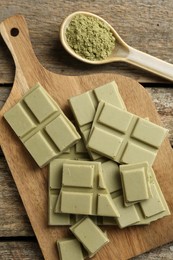 Photo of Pieces of tasty matcha chocolate bar and powder in spoon on wooden table, flat lay