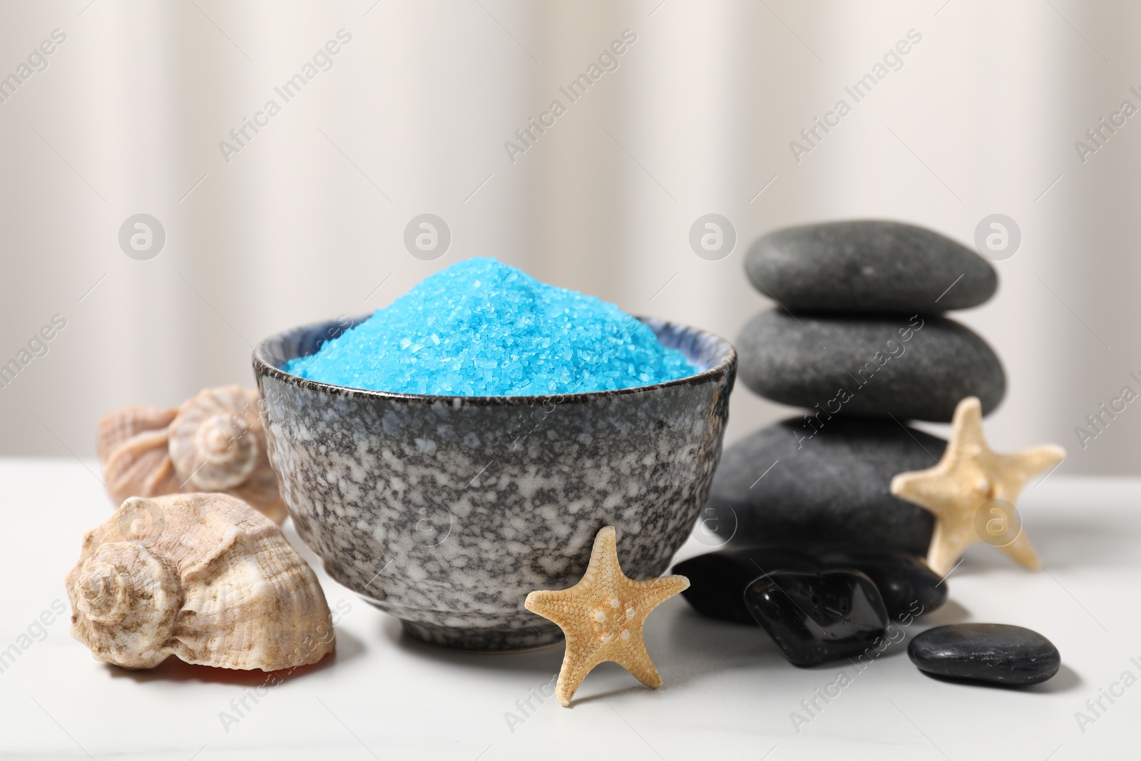 Photo of Light blue sea salt in bowl, spa stones, starfishes and shells on white table, closeup