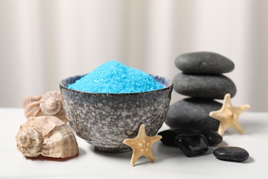 Light blue sea salt in bowl, spa stones, starfishes and shells on white table, closeup