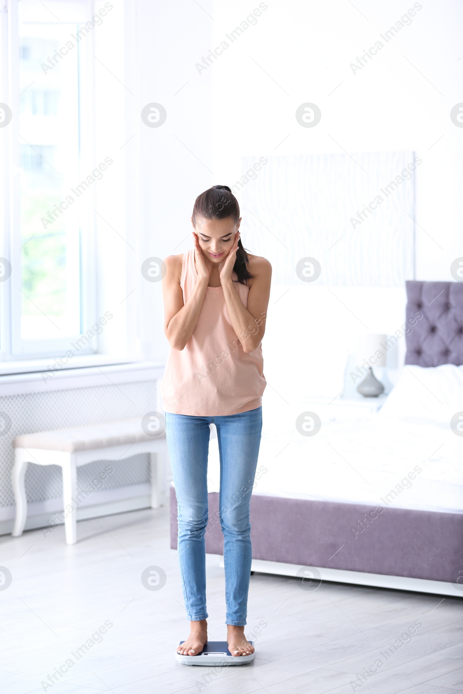 Photo of Surprised young woman measuring her weight using scales at home. Weight loss motivation