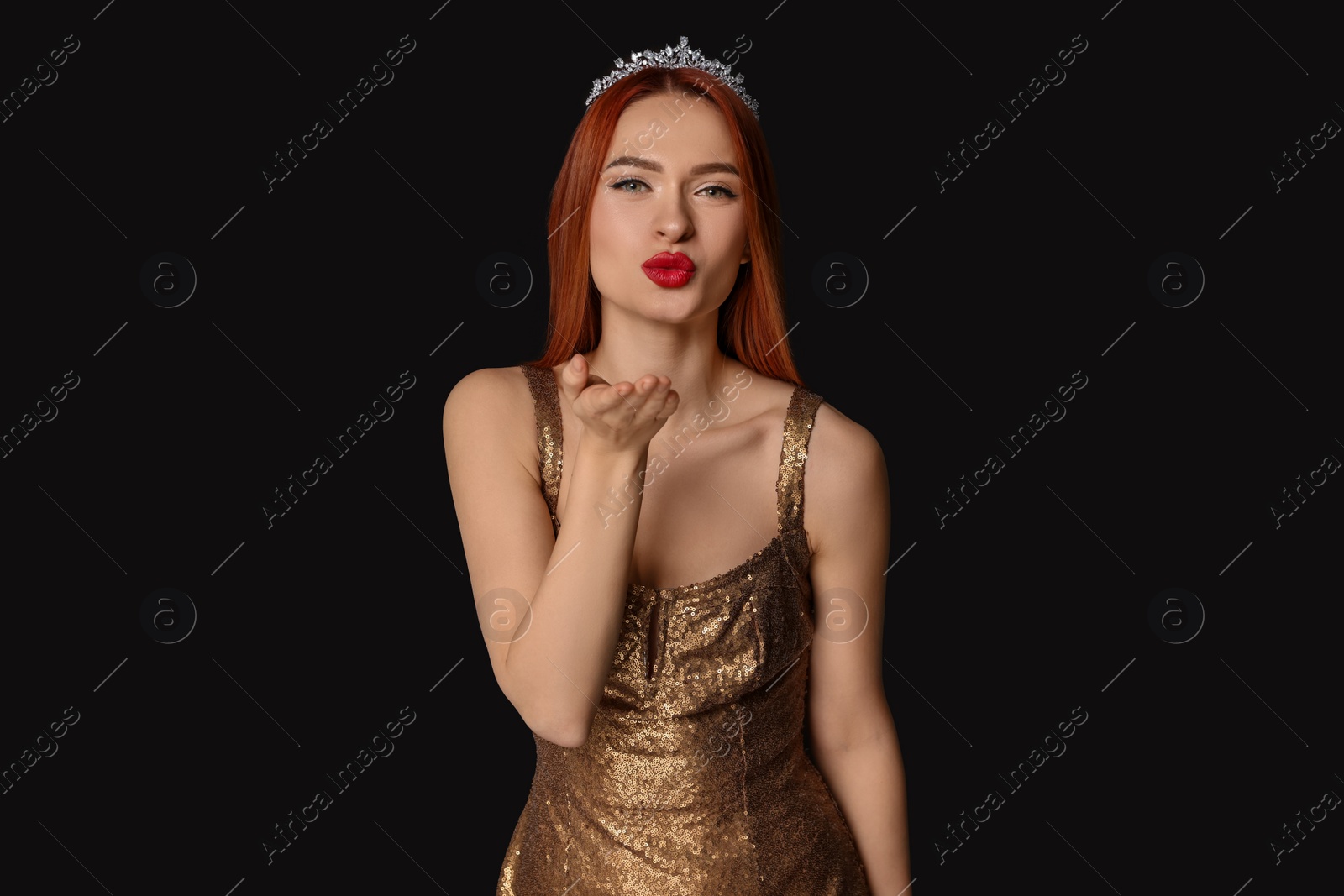 Photo of Beautiful young woman with tiara in dress blowing kiss on black background