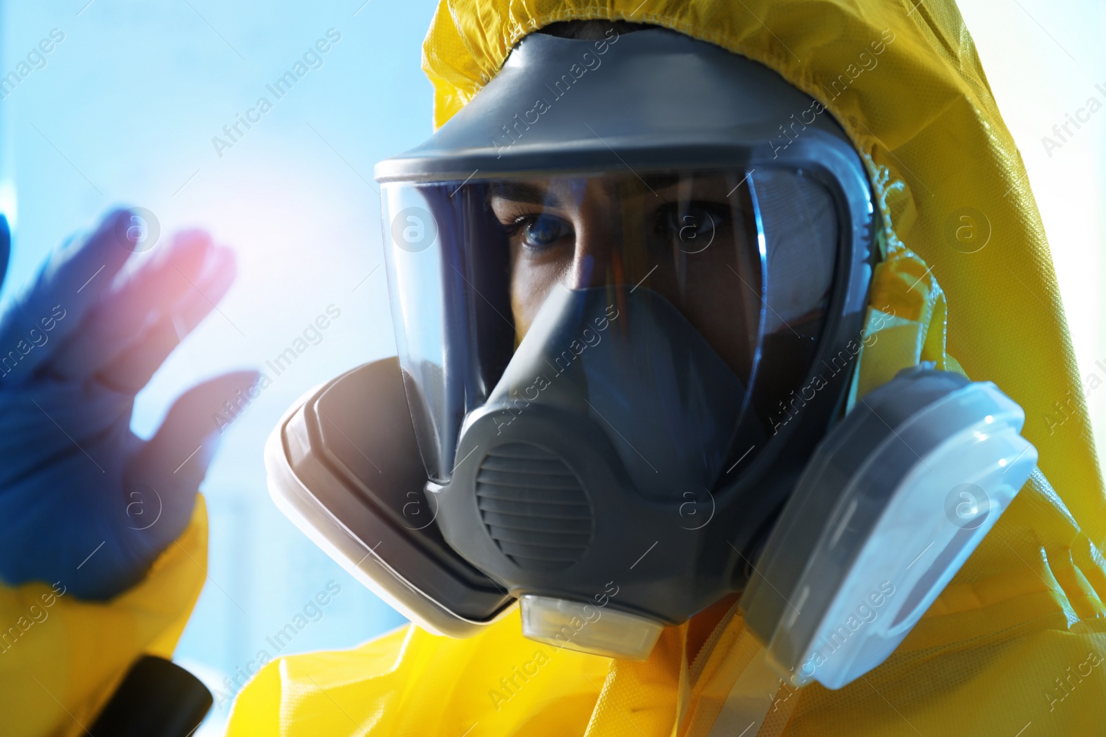 Photo of Scientist in chemical protective suit with microscope slide on light blue background, closeup. Virus research