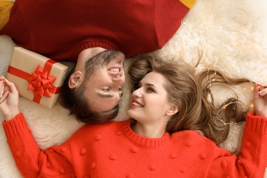 Photo of Happy young couple lying on floor with Christmas gift box at home