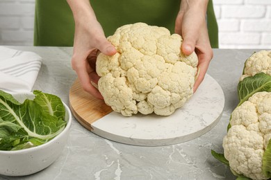 Woman with fresh cauliflower at light grey table, closeup