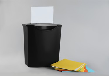 Photo of Shredder with sheet of paper and colorful folders on grey background. Space for text