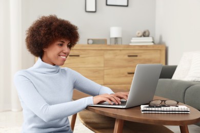 Photo of Beautiful young woman using laptop at wooden coffee table in room