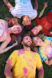 Photo of Happy friends covered with colorful powder dyes on green grass outdoors, above view. Holi festival celebration
