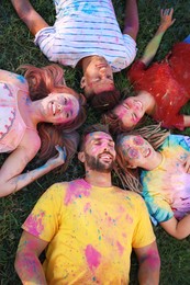 Happy friends covered with colorful powder dyes on green grass outdoors, above view. Holi festival celebration