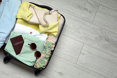 Open suitcase with clothes and accessories on floor, top view. Space for text