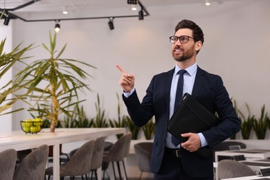 Happy real estate agent with leather portfolio pointing indoors