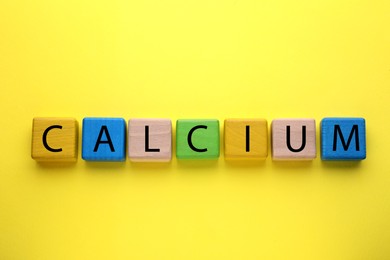 Word Calcium made of colorful wooden cubes with letters on yellow background, flat lay