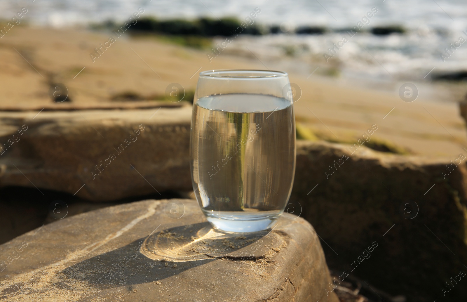 Photo of Glass of fresh water on stone near sea