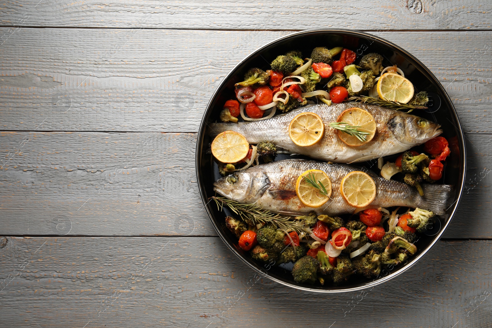 Photo of Baked fish with vegetables, rosemary and lemon on grey wooden table, top view. Space for text