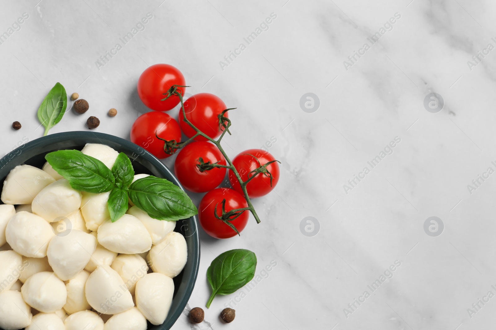 Photo of Delicious mozzarella balls in bowl, tomatoes and peppercorns on white marble table, flat lay. Space for text