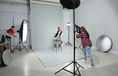 Professional photographer with assistant taking picture of young man in modern studio