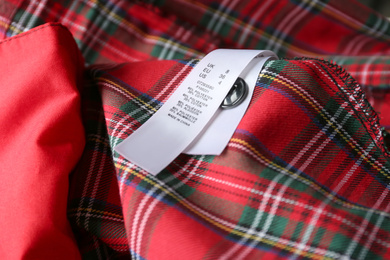 Photo of Clothing label with size and content information on red plaid garment, closeup