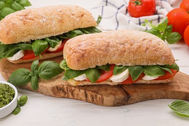 Photo of Delicious Caprese sandwiches with mozzarella, tomatoes and basil on white wooden table