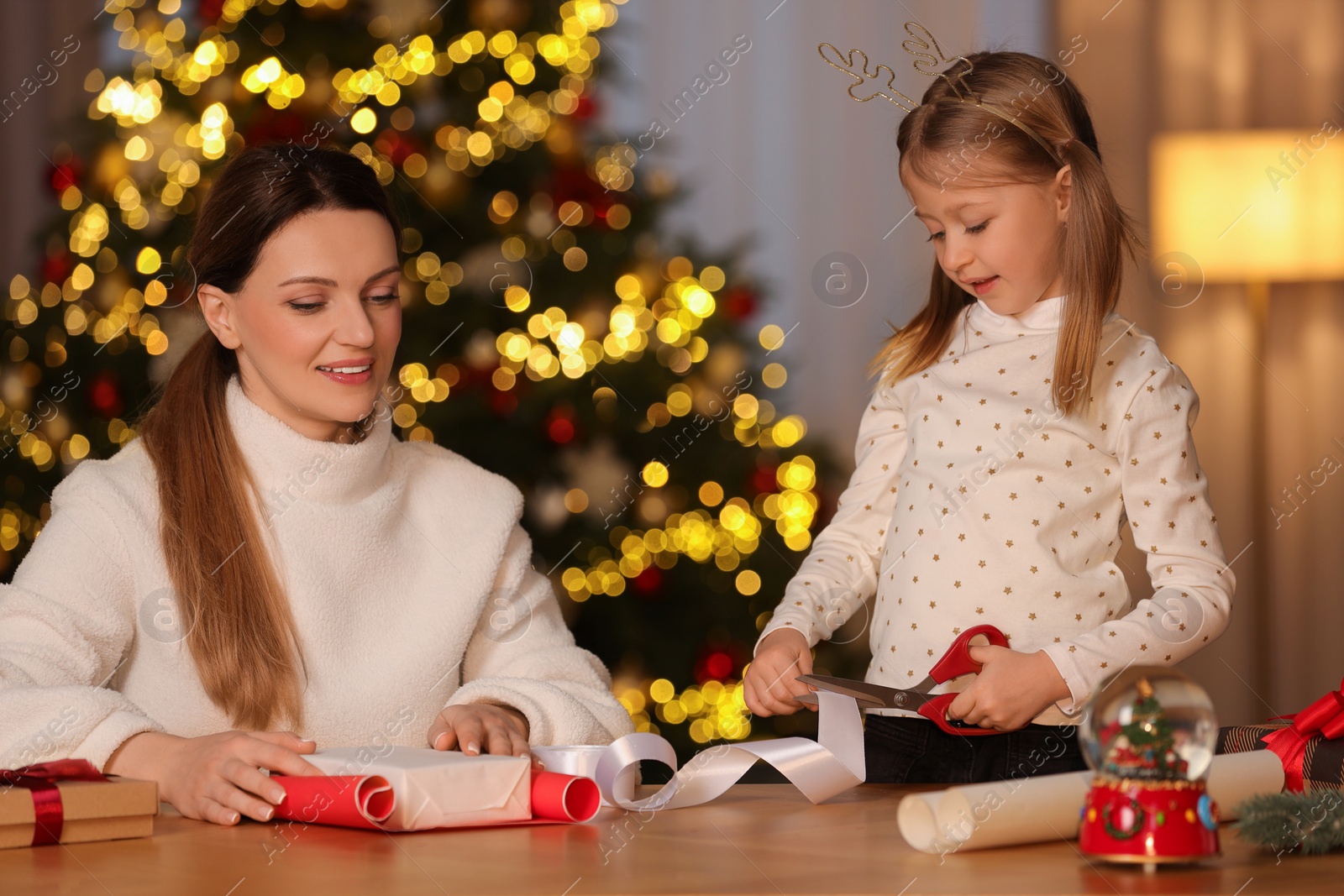 Photo of Christmas presents wrapping. Mother and her little daughter decorating gift box with ribbon at home