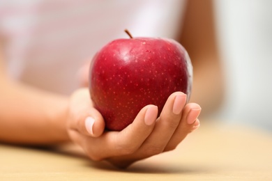 Photo of Woman holding fresh red apple at table, closeup