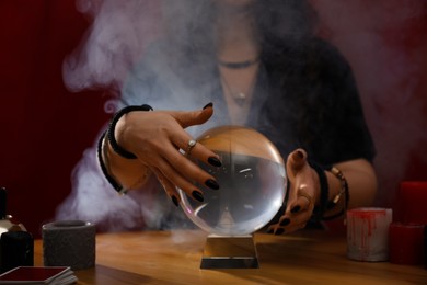 Photo of Soothsayer using crystal ball to predict future at table indoors, closeup