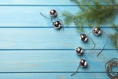 Silver sleigh bells with rope and fir branch on light blue wooden background, flat lay. Space for text