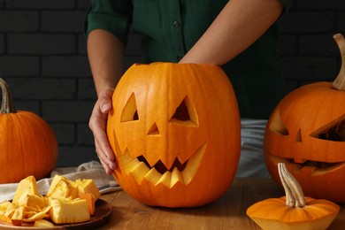 Photo of Woman carving pumpkin for Halloween at wooden table, closeup