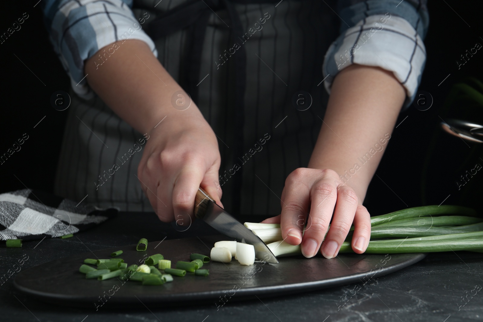 Photo of Woman cutting green spring onions at black table, closeup