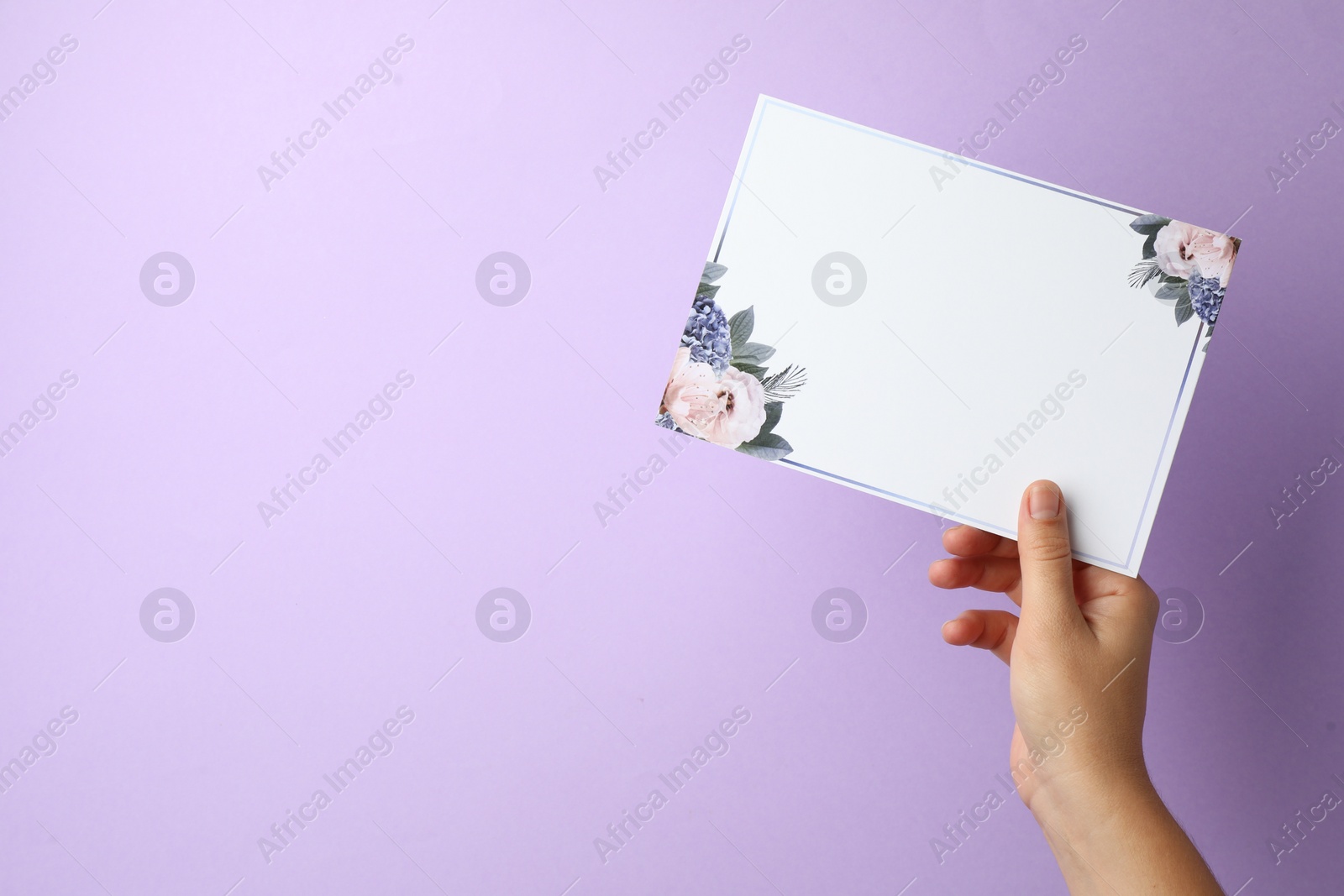 Photo of Woman holding blank invitation card on lilac background, closeup. Space for text