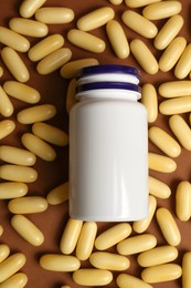 Photo of Plastic medicine bottle surrounded by pills on brown background, flat lay