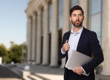 Lawyer with laptop near building outdoors, space for text